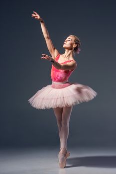 Portrait of the ballerina in ballet pose on a grey background. Ballerina is wearing  pink tutu and pointe shoes