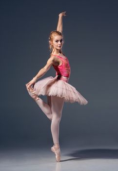 Portrait of the ballerina in ballet pose on a grey background. Ballerina is wearing  pink tutu and pointe shoes