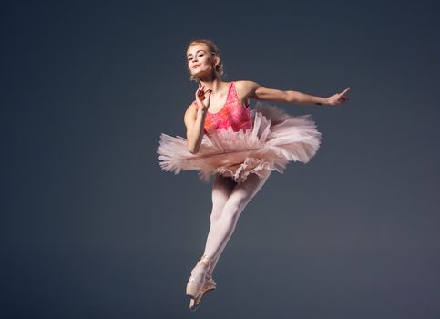 Beautiful female ballet dancer on a grey background. Ballerina is wearing  pink tutu and pointe shoes