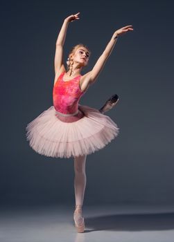 Portrait of the ballerina in ballet pose on a grey background. Ballerina is wearing  pink tutu and pointe shoes