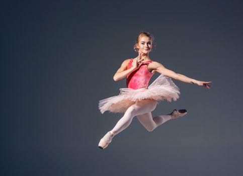 Beautiful female ballet dancer on a grey background. Ballerina is wearing  pink tutu and pointe shoes