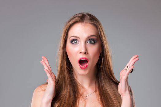 Close-up portrait of surprised beautiful girl holding her head in amazement and open-mouthed. Over gray background.