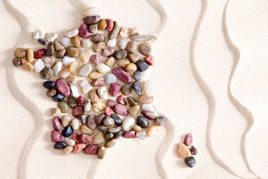 Conceptual map of France and Corsica formed of colorful waterwashed pebbles of quartzite, agate, jasper, and dolomite on white bach sand with an undulating wavy pattern