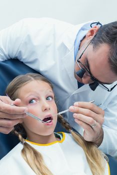 Male dentist examining girls teeth in the dentists chair