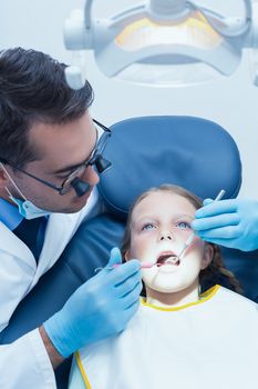 Male dentist examining girls teeth in the dentists chair