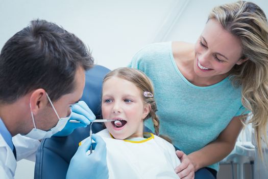 Dentist examining girls teeth in the dentists chair with assistant