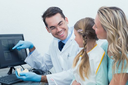 Male dentist with assistant showing little girl her mouth x-ray on computer