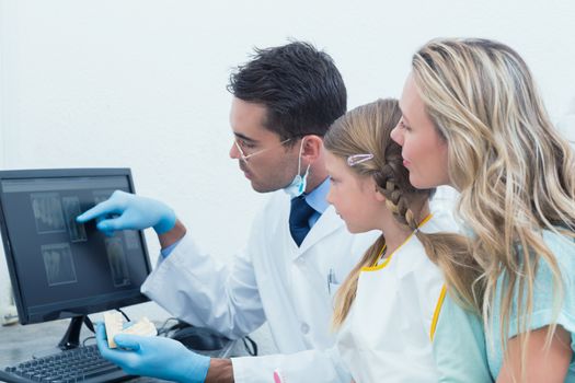 Male dentist and assistant showing little girl her mouth x-ray on computer