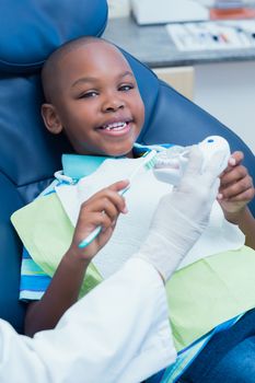 Dentist teaching happy boy how to brush teeth in the dentists chair