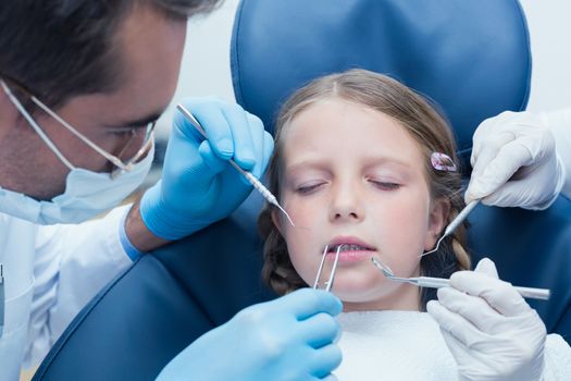 Dentist with assistant examining girls teeth in the dentists chair