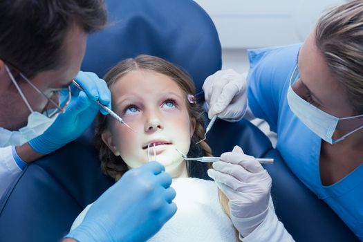 Dentist with assistant examining girls teeth in the dentists chair