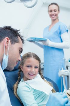 Male dentist teaching girl how to brush teeth in the dentists chair