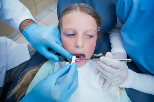 Dentist with assistant examining girls teeth in the dentists chair