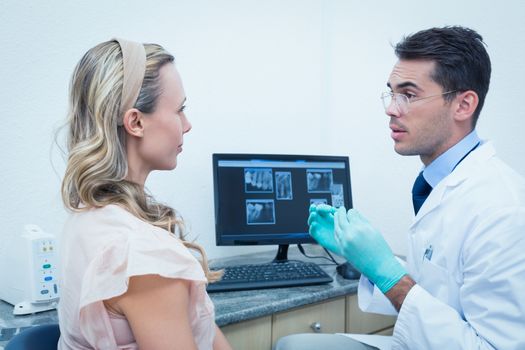 Side view of male dentist showing woman her mouth x-ray on computer