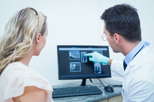 Side view of male dentist showing woman her mouth x-ray on computer