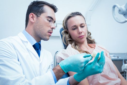 Male dentist teaching woman how to brush teeth in the dentists chair