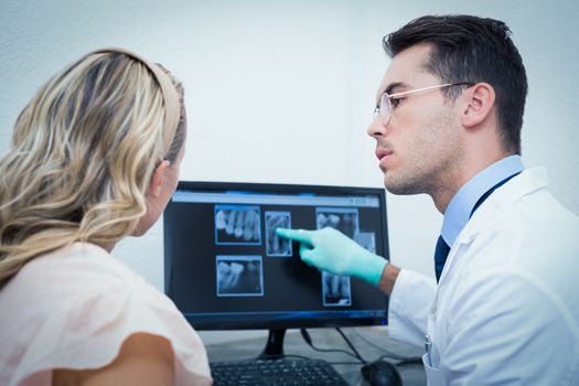 Side view of male dentist showing woman her mouth x-ray on computer