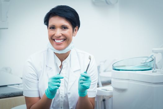 Portrait of happy confident female dentist holding dental tools