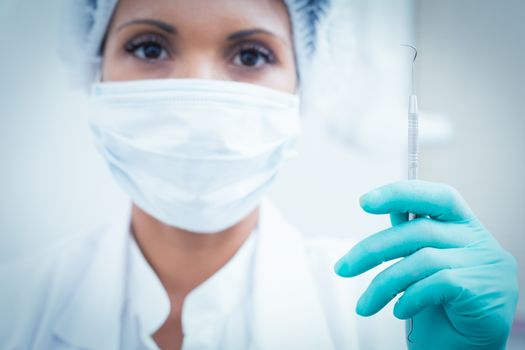 Portrait of female dentist in surgical mask holding hook