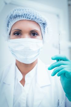 Portrait of female dentist in surgical mask holding hook