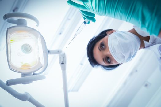 Low angle view of female dentist in surgical mask holding injection
