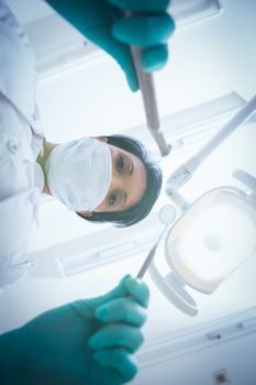 Portrait of female dentist in surgical mask holding dental tools