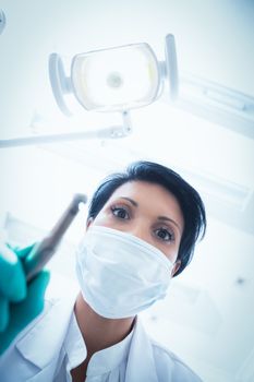 Low angle view of female dentist in surgical mask holding dental drill