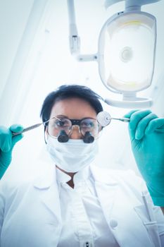 Low angle view of female dentist in surgical mask holding dental tools