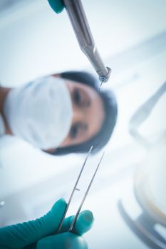 Low angle view of female dentist in surgical mask holding dental tools