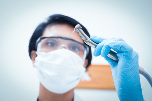 Portrait of female dentist in surgical mask holding dental drill