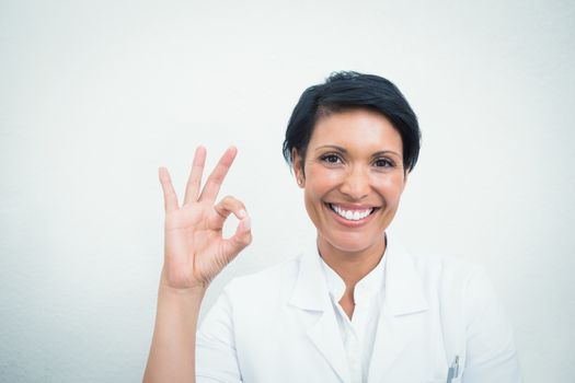 Portrait of smiling female dentist gesturing okay sign over white background