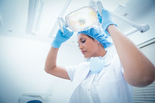 Low angle view of serious female dentist adjusting light
