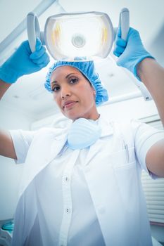 Portrait of serious female dentist adjusting light