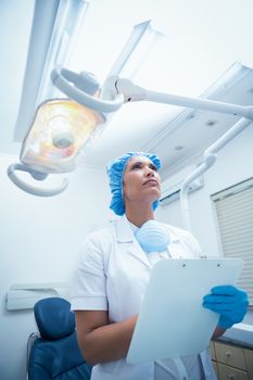 Serious female dentist with clipboard looking up