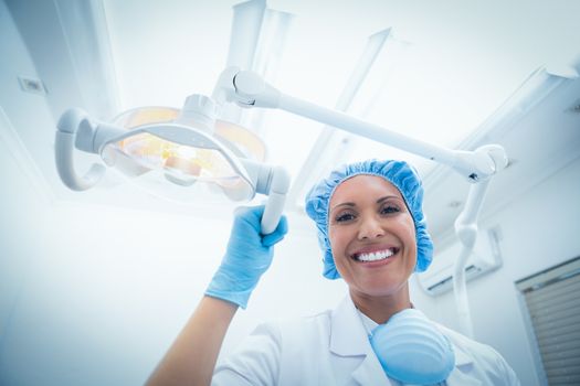 Low angle portrait of smiling female dentist adjusting light