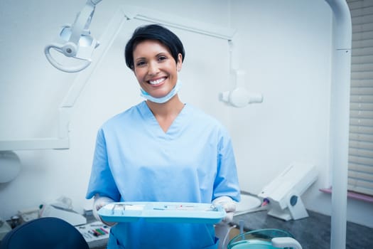 Portrait of female dentist in blue scrubs holding tray of tools