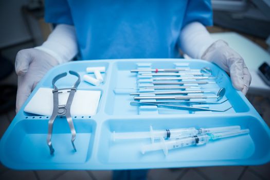 Close up mid section of female dentist in blue scrubs holding tray of tools