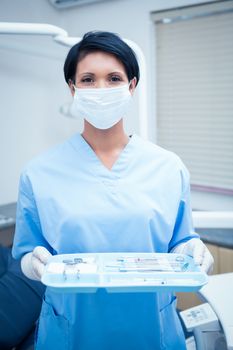 Portrait of female dentist in blue scrubs holding tray of tools