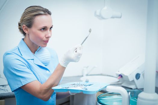 Serious young female dentist holding dental tool
