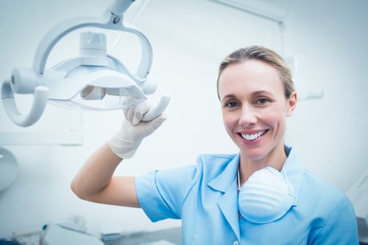 Portrait of smiling young female dentist adjusting light