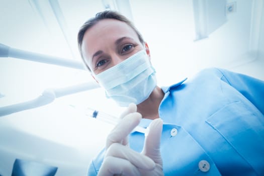 Low angle portrait of female dentist in surgical mask holding injection