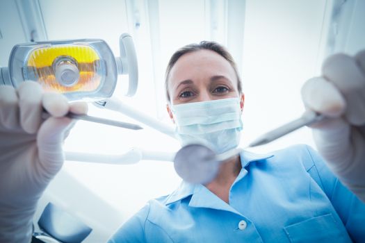 Low angle portrait of female dentist in surgical mask holding dental tools