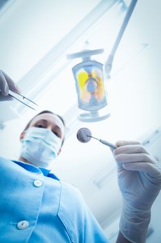 Low angle portrait of female dentist in surgical mask holding dental tools