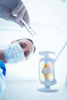 Low angle portrait of female dentist in surgical mask holding dental tool