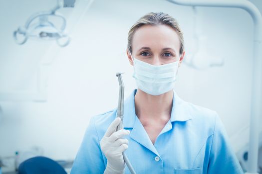 Portrait of female dentist in surgical mask holding dental tool