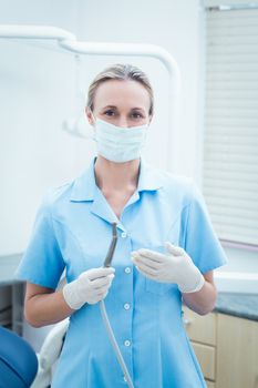 Portrait of female dentist in surgical mask holding dental tool