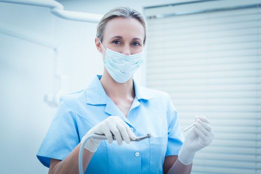 Portrait of female dentist in surgical mask holding dental tools