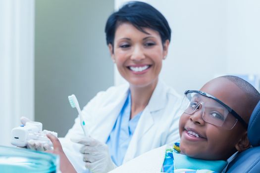 Female dentist teaching boy how to brush teeth in the dentists chair