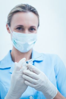 Portrait of young female dentist in surgical mask holding injection