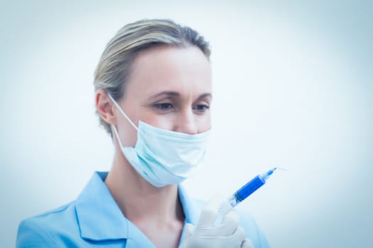 Portrait of young female dentist in surgical mask holding injection